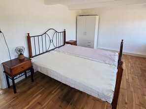 Ein Schlafzimmer mit Holzboden, einem Bett mit Metallkopfteil, einem Nachttisch mit Lampe und einem Kleiderschrank.