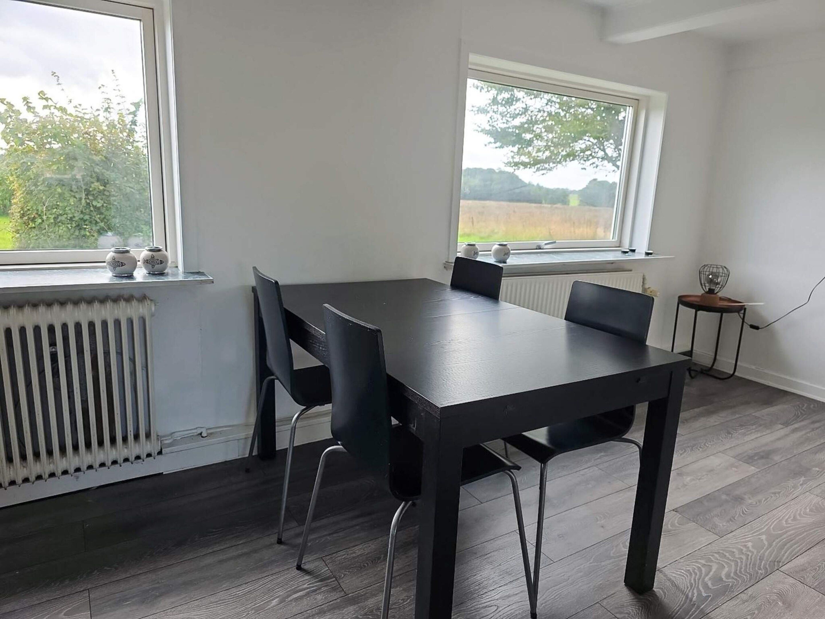 Une pièce avec une grande table et des chaises, un radiateur et une fenêtre donnant sur des arbres et des champs.