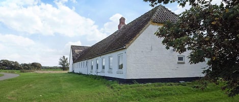 A long white building with a steeply pitched roof, surrounded by a grassy field.