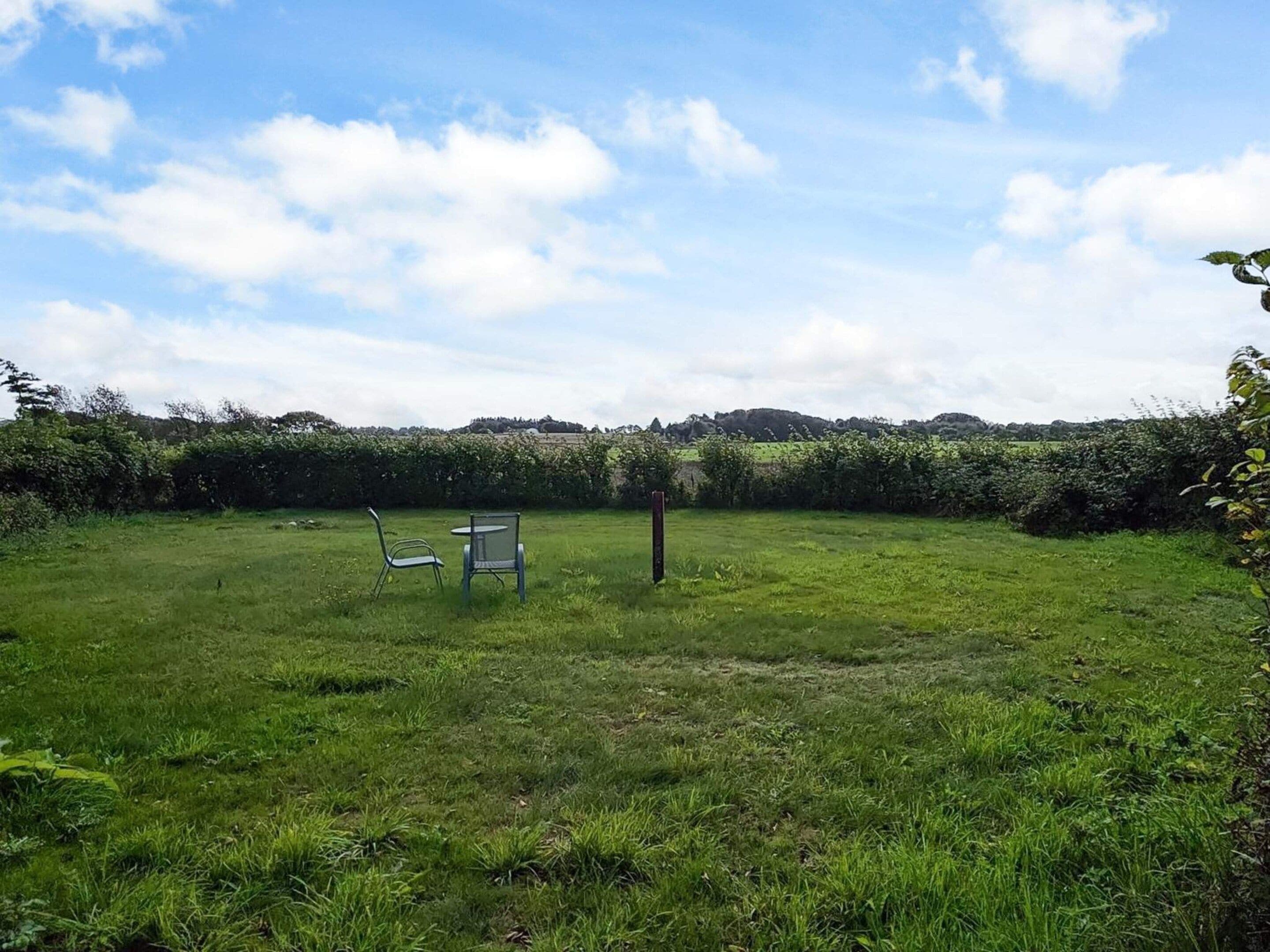 Un espace extérieur recouvert d’herbe, avec deux chaises en métal et un poteau en bois.