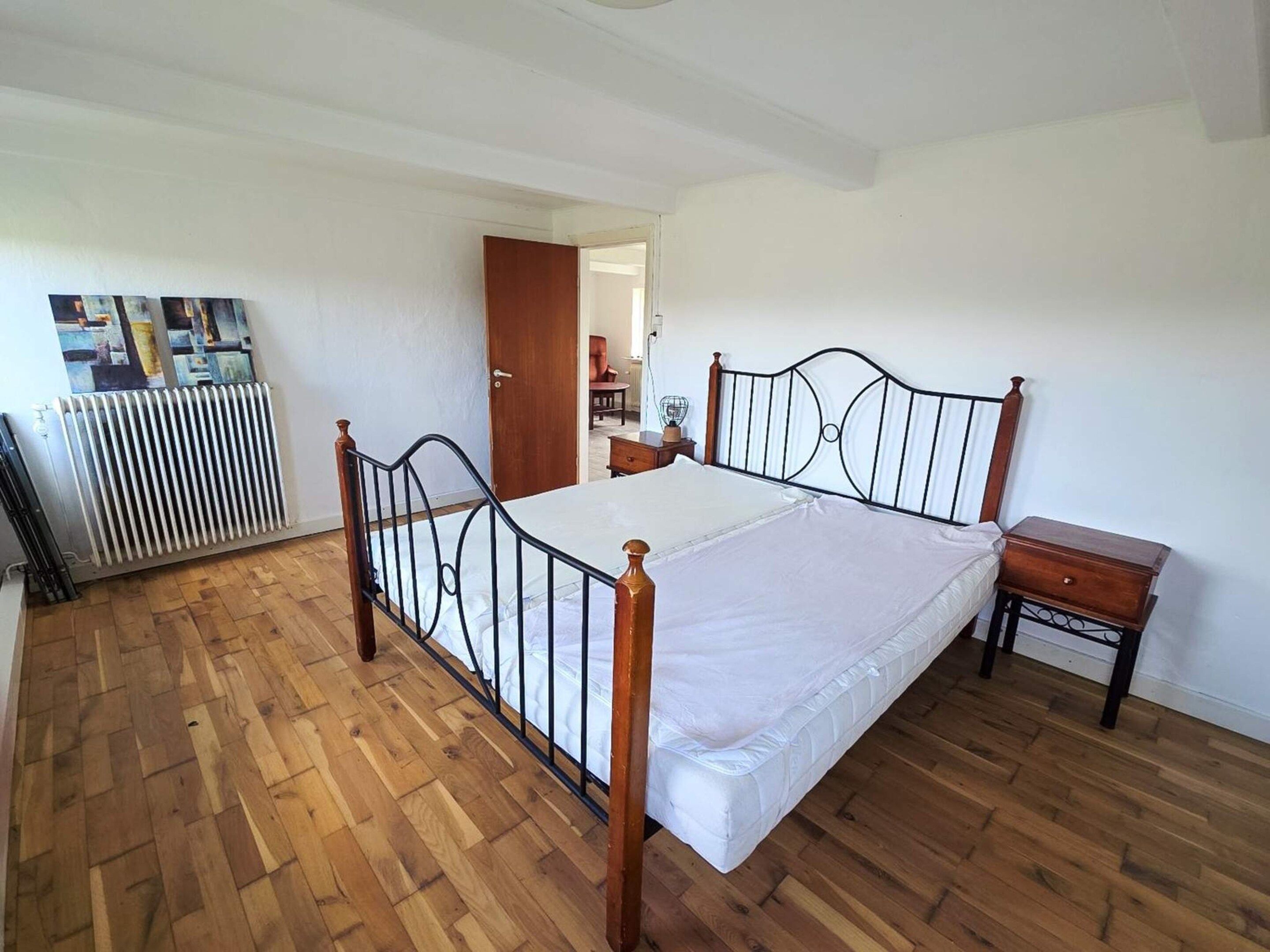 Ein Schlafzimmer mit Holzboden, einem Metallbett, einem Nachttisch und einer Heizung.