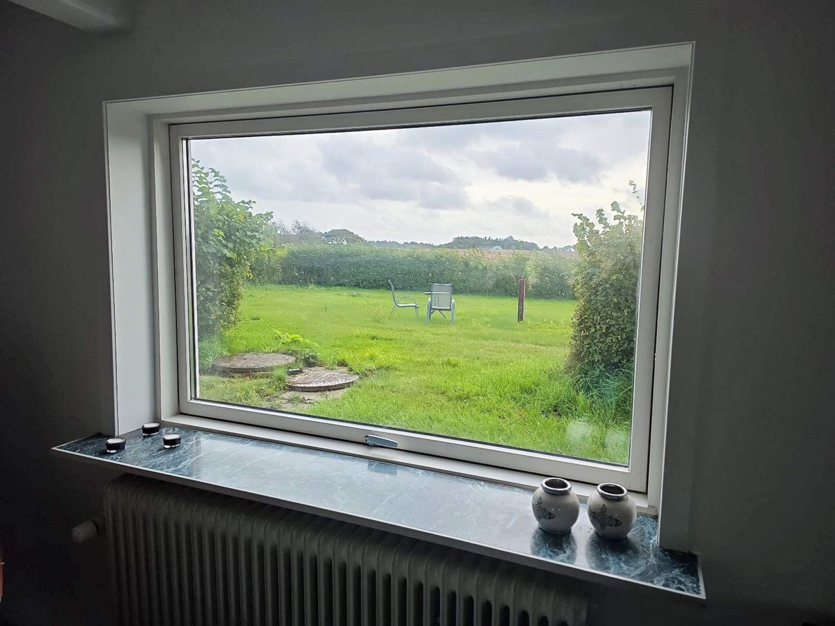 Een raam met uitzicht op een grasveld en een bord, een radiator onder het raam, en twee kleine vazen op de vensterbank.