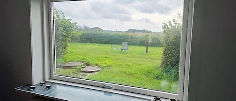 A window with a view of a grassy field and a signpost, a radiator below, and two small vases on the sill.