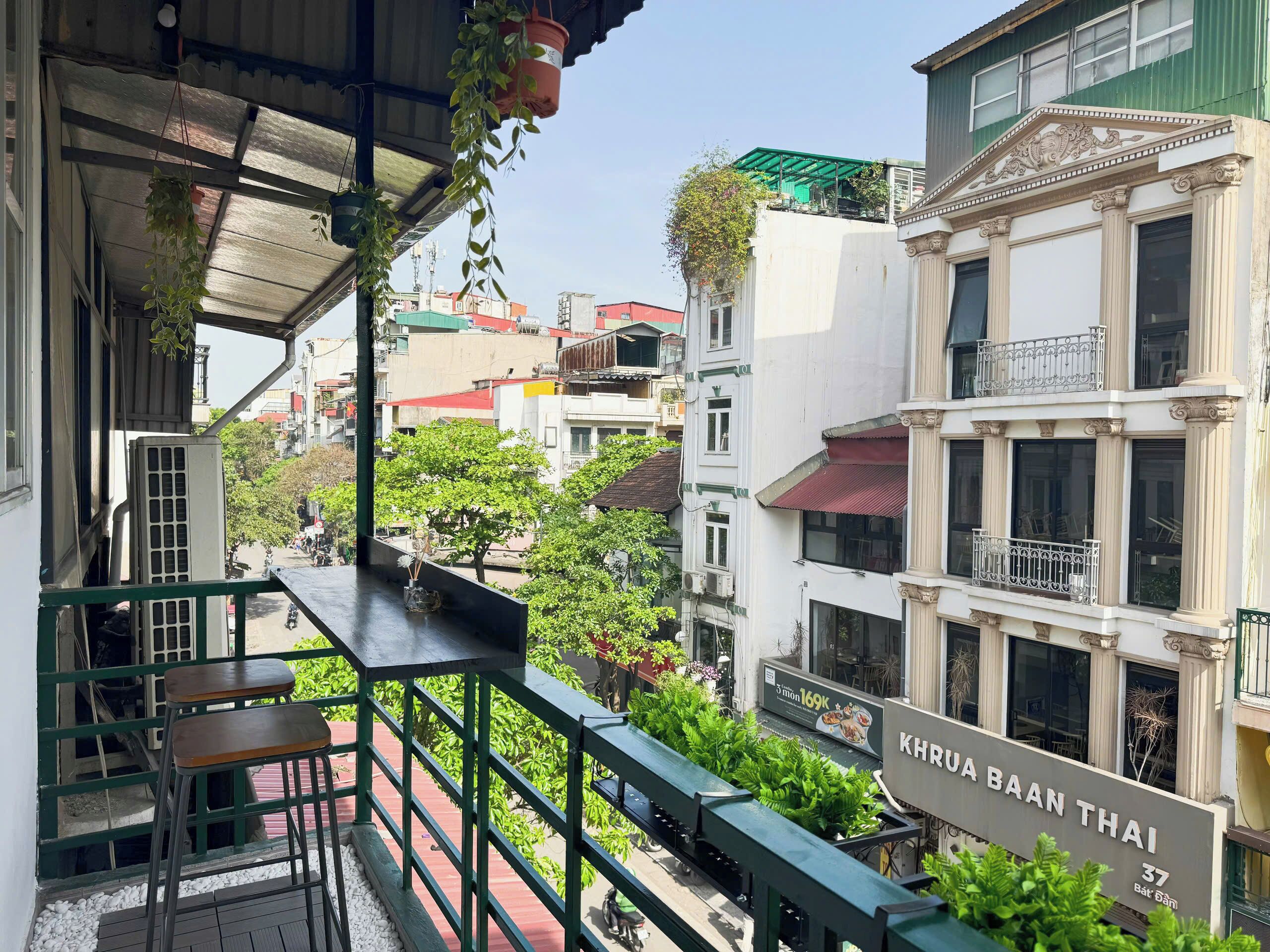Un balcón con vista a la calle, un letrero que dice 'KHRUA BAAN THAI' y un edificio de arquitectura clásica.