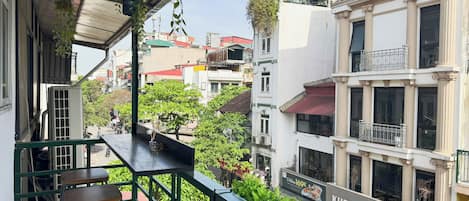 A balcony with a view of a street, a sign for 'KHRUA BAAN THAI', and a building with classical architecture.