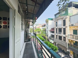Ein Balkon mit Blick auf eine Straße, gegenüber ein Restaurant namens 'KHRUA BAAN THAI' und ein Gebäude mit der Aufschrift 'EMINEM'.