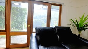 Una stanza con un divano in pelle nera, una pianta in vaso e una porta scorrevole in vetro che dà su una zona esterna.