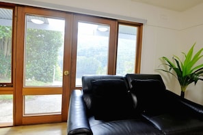 Ein Zimmer mit einer schwarzen Ledersofa, einem Blumentopf und einer Schiebetür zu einem Außenbereich.