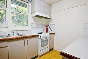 Eine Küche mit Herd, Backofen und Spüle. Ein Fenster bietet Blick auf Grünflächen.
