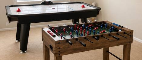 A room with a foosball table and a table tennis table.