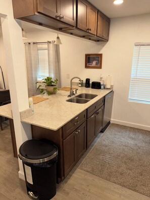 A kitchen with a granite countertop, stainless steel sink, and wooden cabinets. -  The Carlton — The perfect retreat to relax and unwind with a Great Location! (Tallahassee)