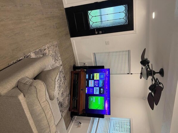 Ein Wohnzimmer mit Fernseher, Deckenventilator und einem Fenster mit Jalousien.