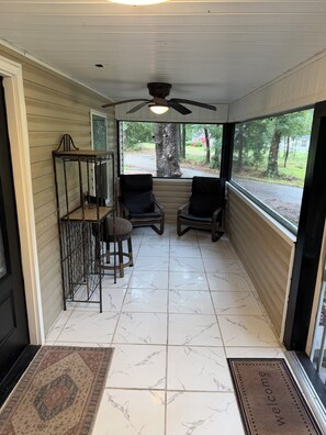 A covered porch with two chairs, a small table, and a ceiling fan. -  The Carlton — The perfect retreat to relax and unwind with a Great Location! (Tallahassee)
