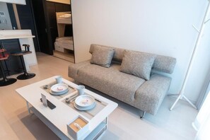 Une chambre moderne avec un canapé gris, une table basse blanche et un lit superposé à l’arrière-plan.