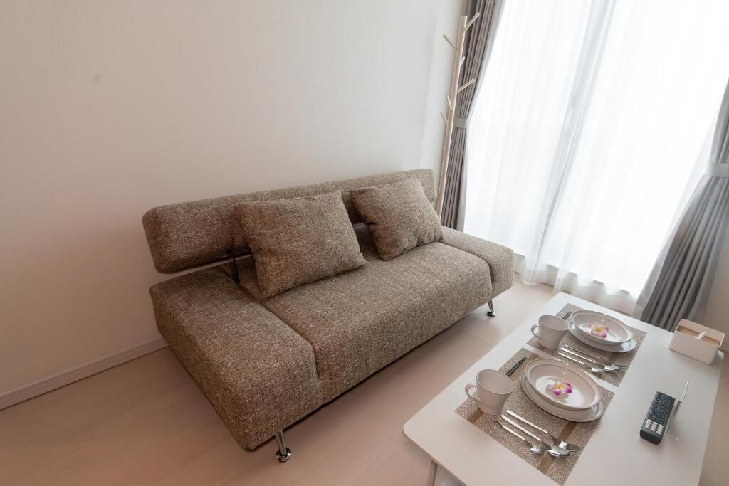 A modern living room with a sofa, a dining table set with plates, cutlery, and a remote control.
