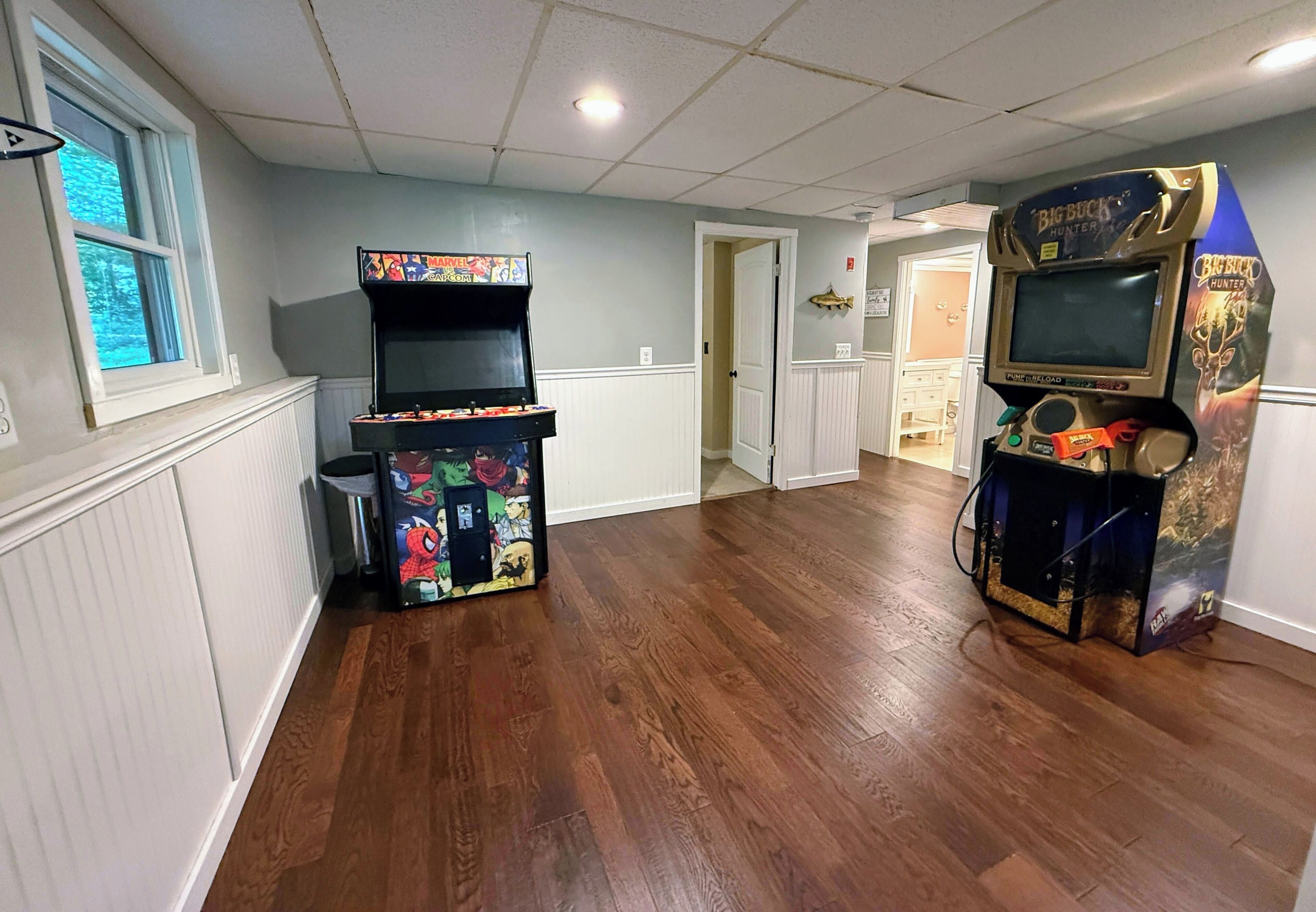 A room with two arcade machines, wooden flooring, and a door leading to another room.