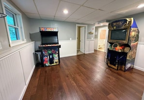 Une pièce avec deux bornes d’arcade, un plancher en bois et une porte donnant sur une autre pièce.