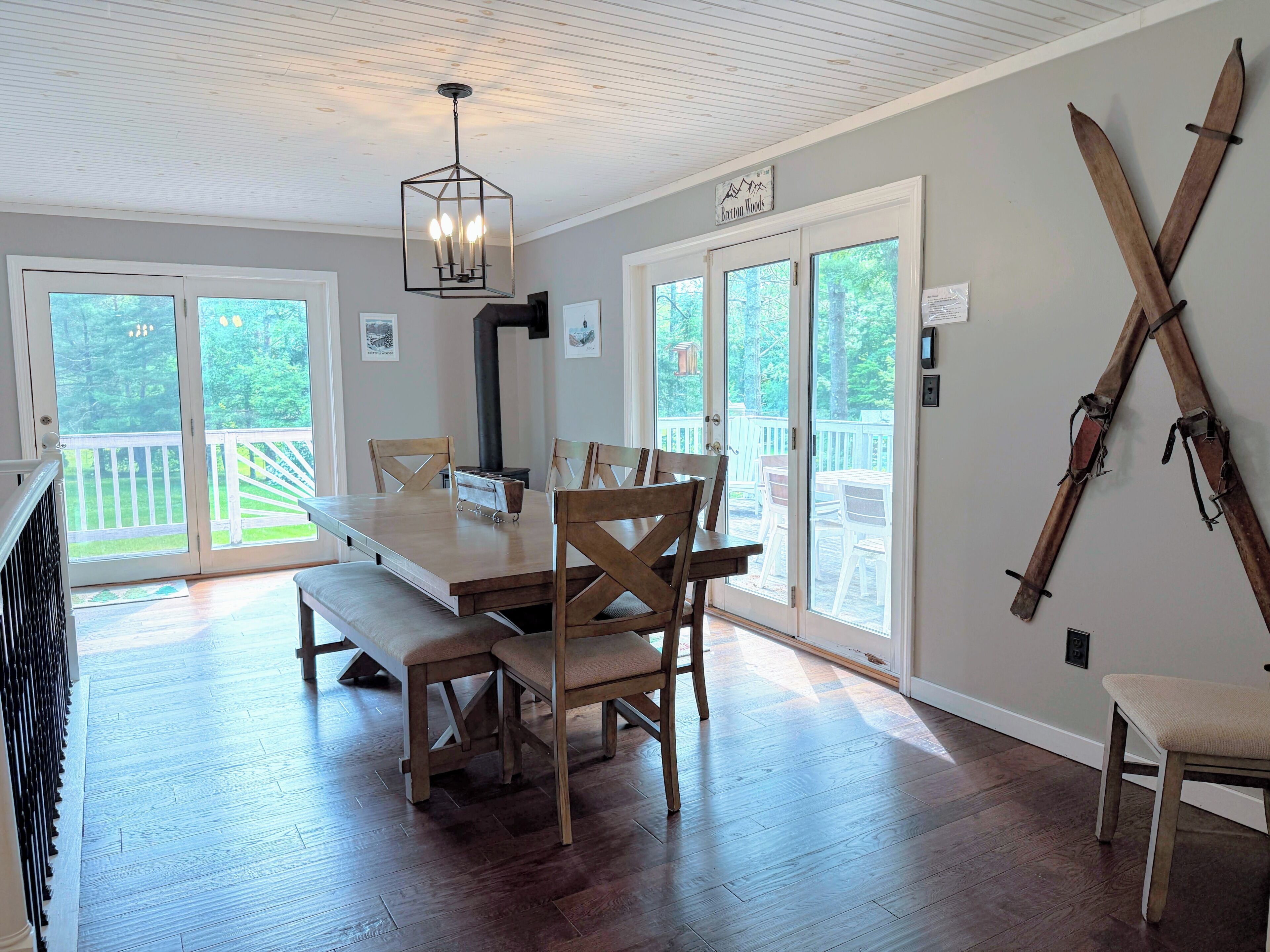 A dining area with a wooden table and chairs, a hanging light fixture, and a view through large sliding glass doors to an outdoor deck.