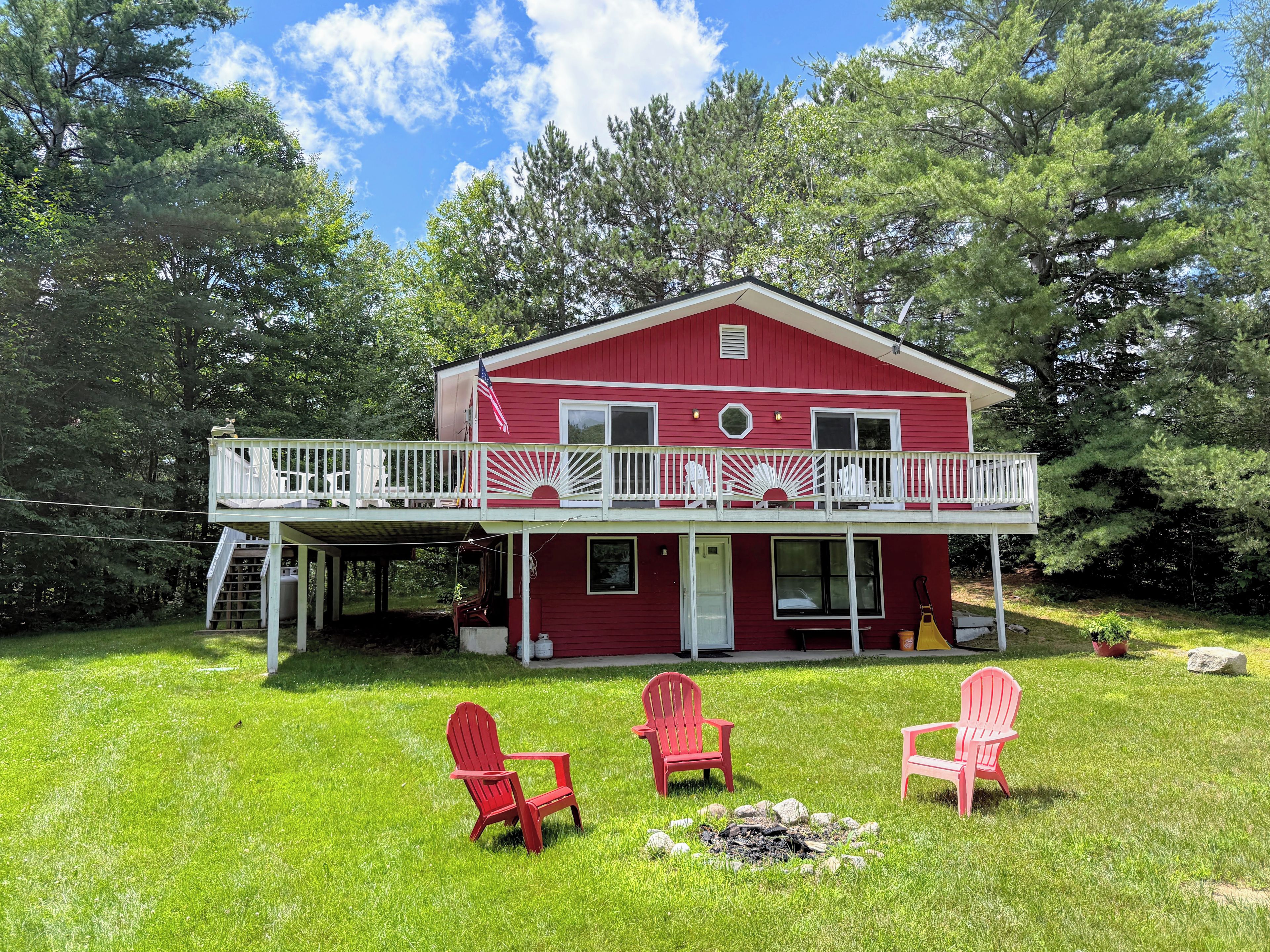 Ein rotes Haus mit Balkon, umgeben von grünem Gras und Bäumen.