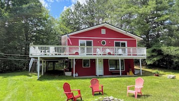 Ein rotes Haus mit Balkon, umgeben von grünem Gras und Bäumen.