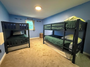 Une chambre avec deux lits superposés, une fenêtre avec des rideaux et un luminaire au plafond.