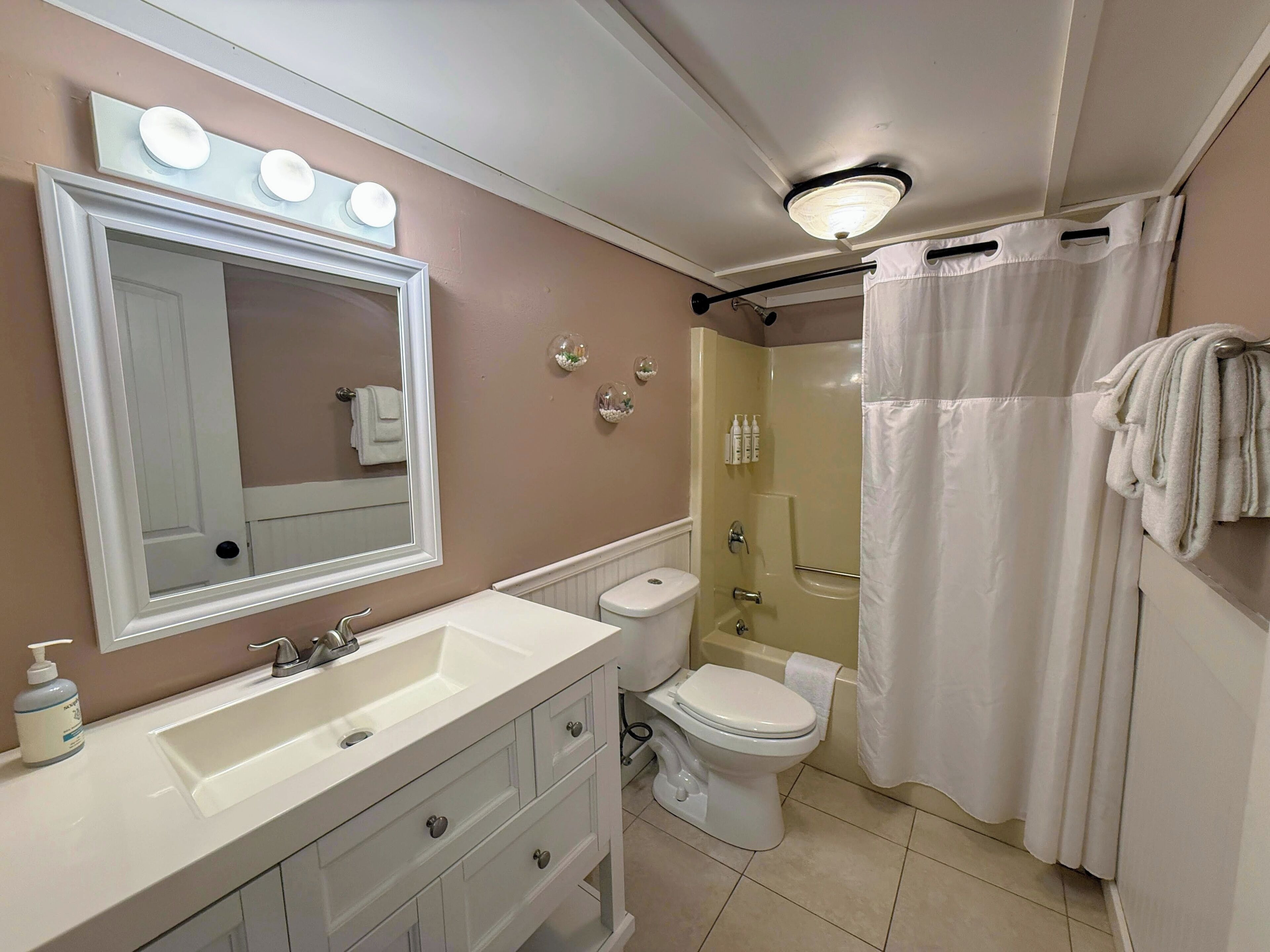 A bathroom with a vanity, a toilet, a shower, and a mirror with lights.