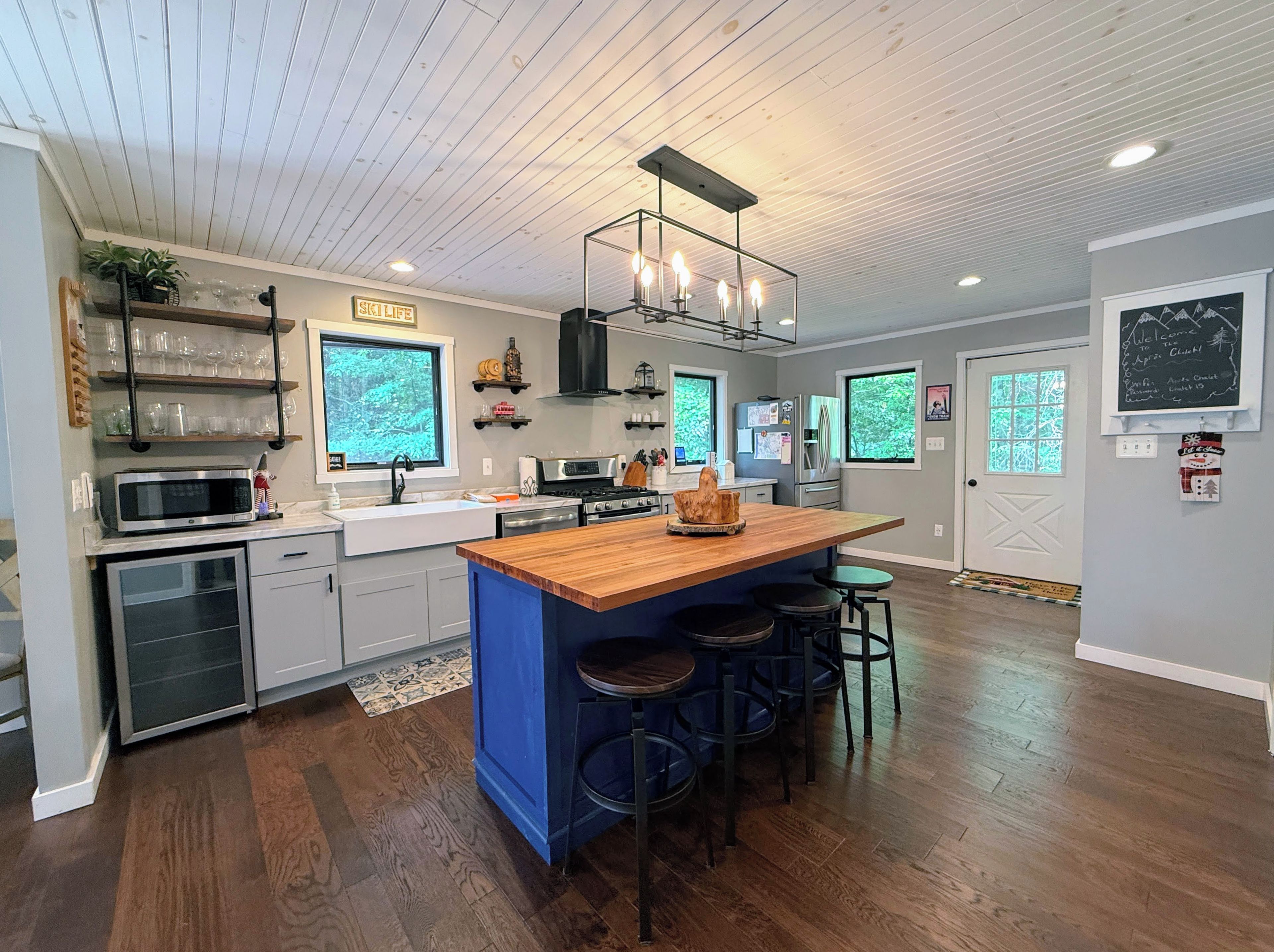 A modern kitchen with a central island, stainless steel appliances, and a wooden ceiling.
