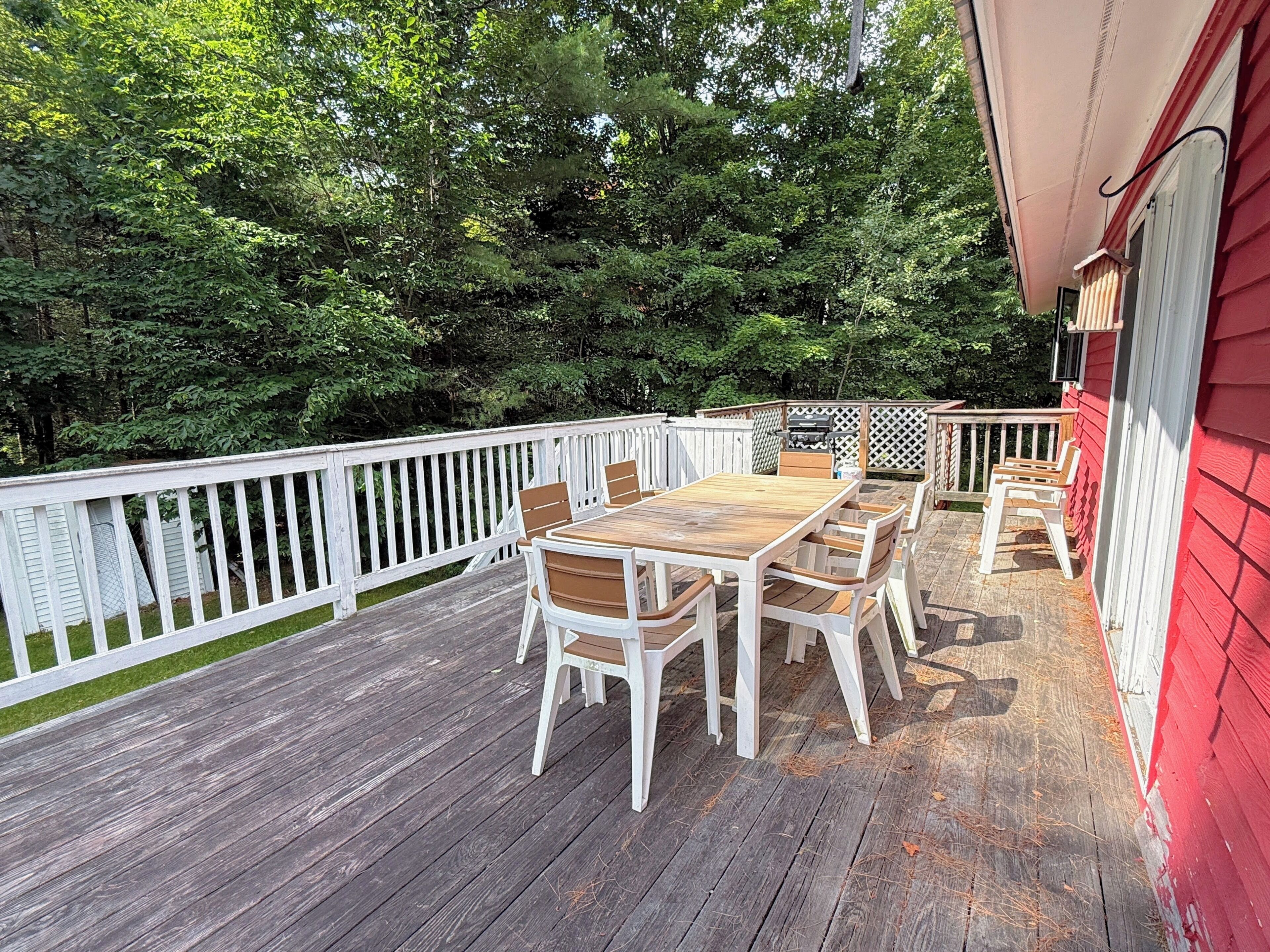 A wooden deck with a white railing, a wooden table, and white chairs.