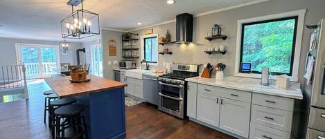 A modern kitchen with a central island, stainless steel appliances, and a large window providing a view of greenery.