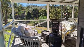 A covered outdoor seating area with two wicker chairs, a grill, and a view of the surrounding landscape.