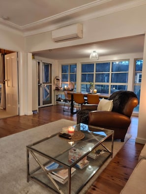 A living room with a glass coffee table, leather sofa, and a dining area with chairs and a table.