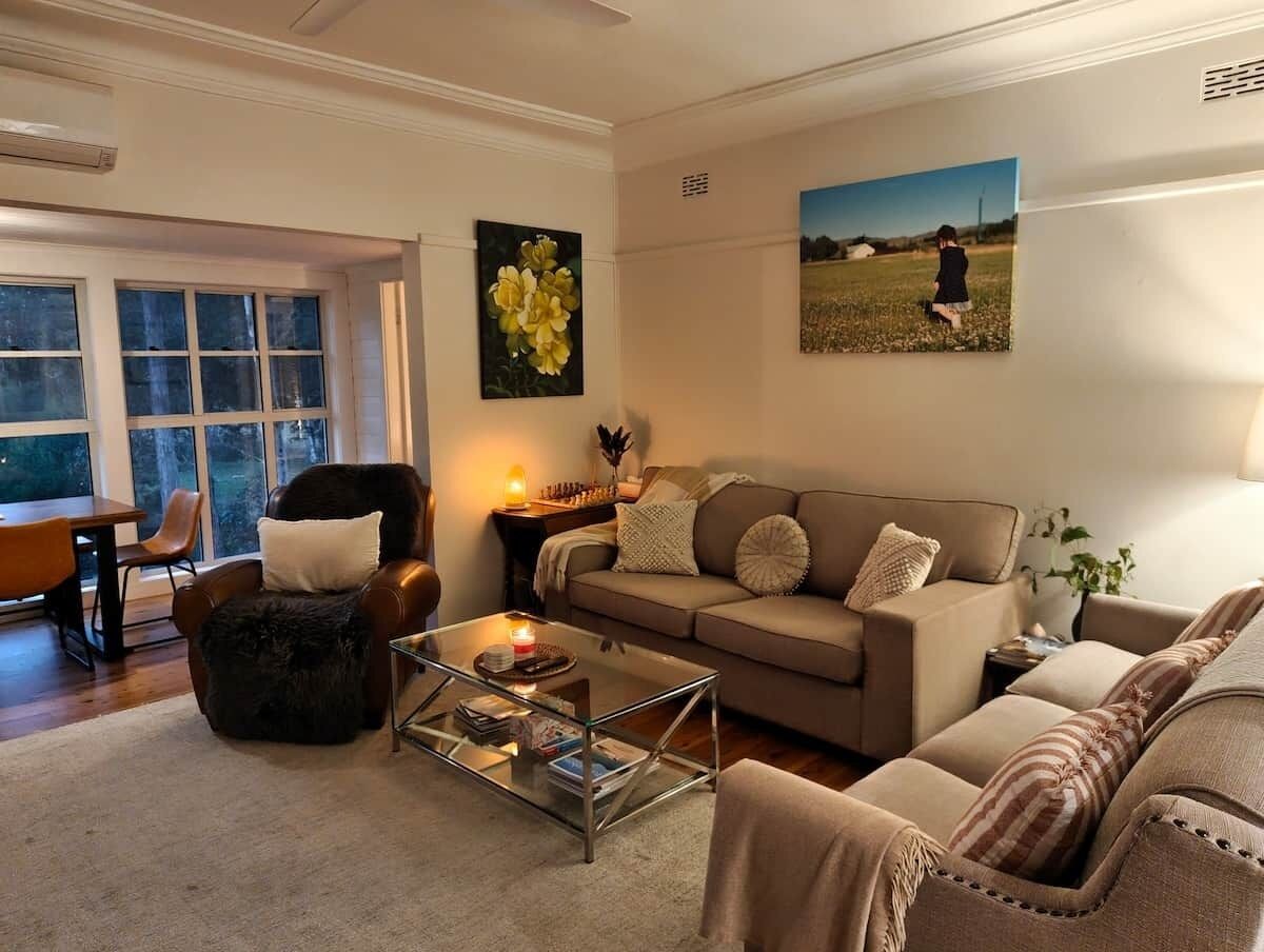 A living room with a sofa, armchair, coffee table, and a painting on the wall.