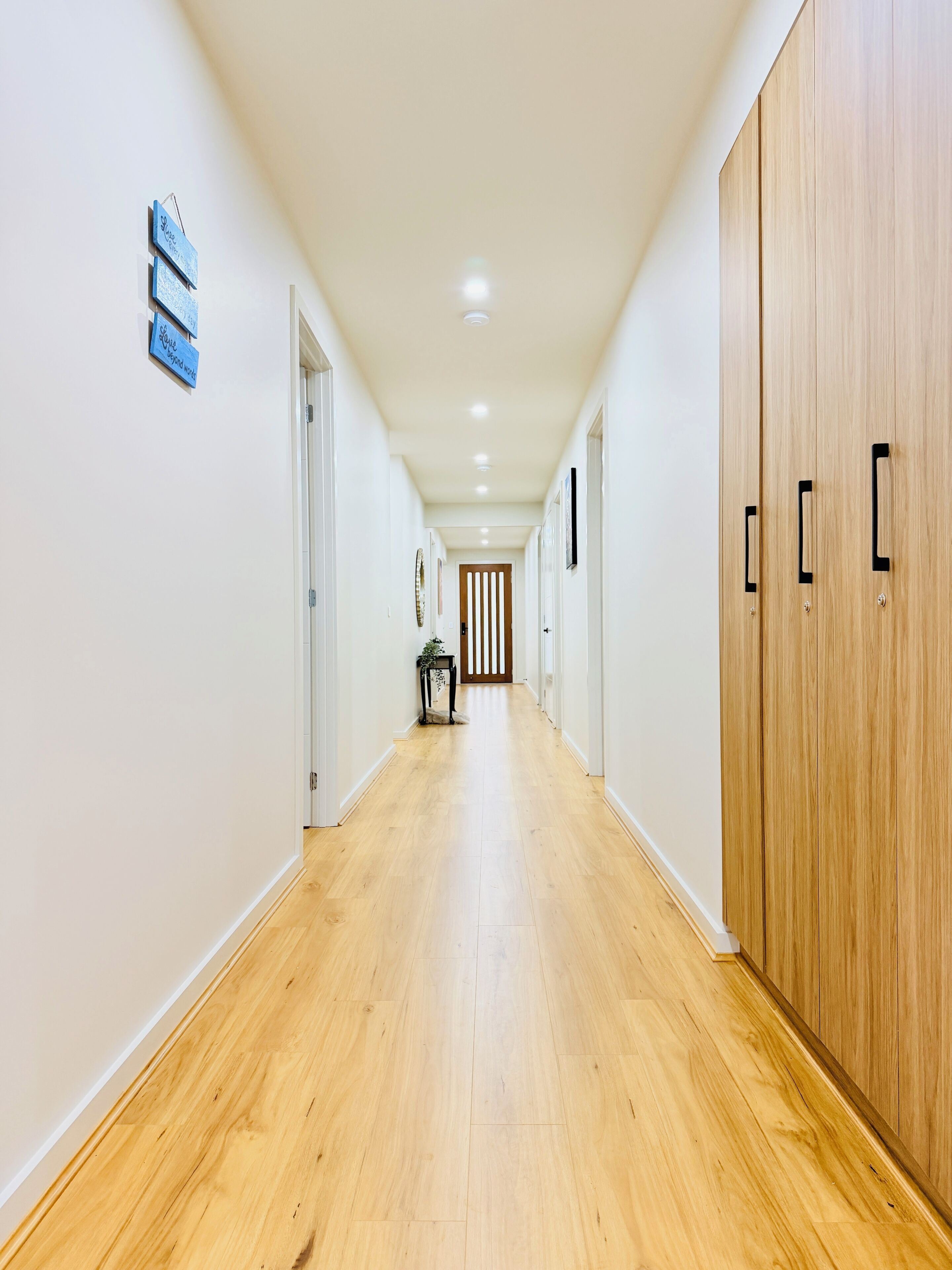 A corridor with wooden flooring, white walls, and a wooden wardrobe on the right.