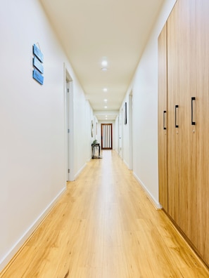 A corridor with wooden flooring, white walls, and a wooden wardrobe on the right.