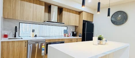 Una cocina moderna con gabinetes de madera, electrodomésticos de acero inoxidable e iluminación colgante.