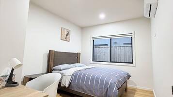 Ein Schlafzimmer mit Bett, Schreibtisch, Stuhl, Fenster und einer Klimaanlage.