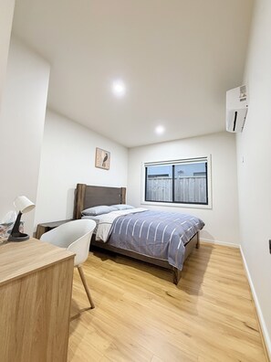 A bedroom with a bed, a desk, a chair, a window, and an air conditioning unit.
