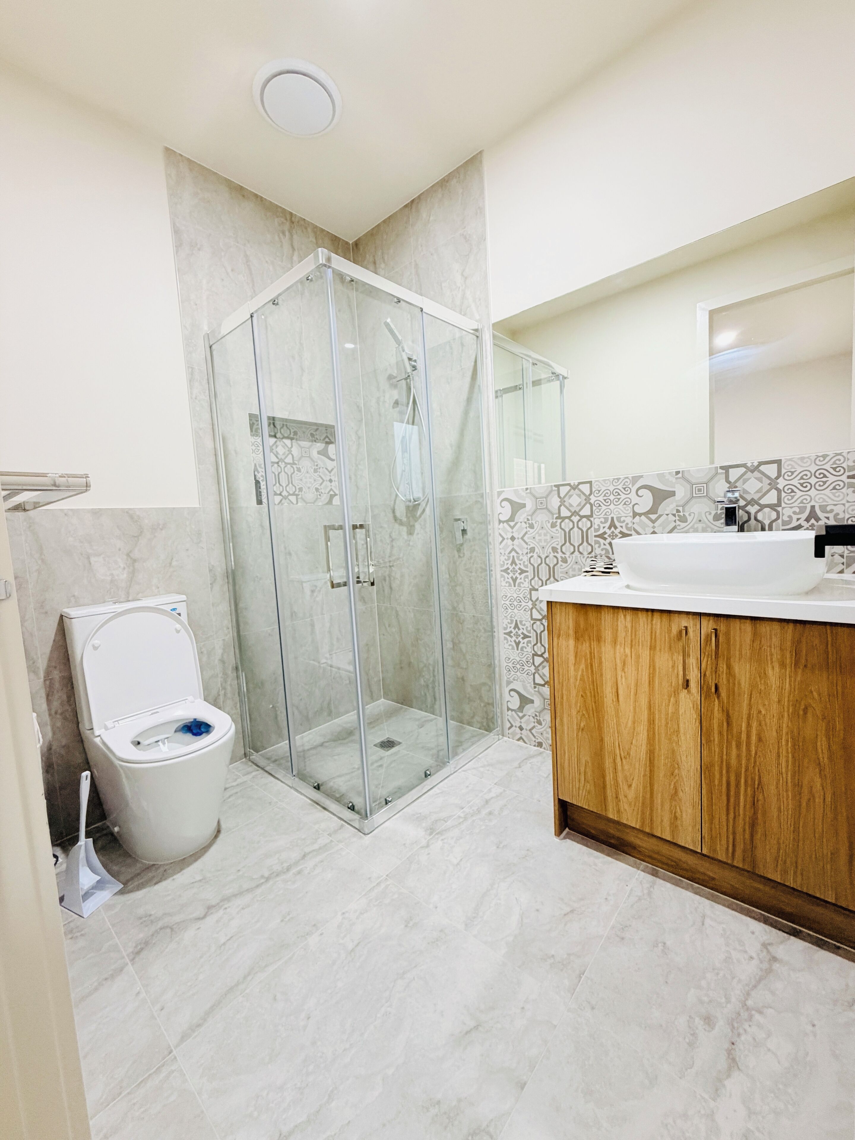 A bathroom with a glass-enclosed shower, a toilet, and a wooden vanity with a sink.