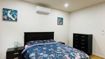 Une chambre à coucher avec une couvre-lit à motifs floraux, une tête de lit noire, une table de chevet avec une lampe et une commode.