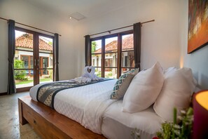 A bedroom with a bed, a wooden bench, and a view of a building through a window. - 7-bedroom private estate in Nusa Dua. Accommodating up to 14 guests with flexible bedding arrangements. Includes daily breakfast, a private chef, airport transfers, complimentary massages, housekeeping, and a dedicated driver. (Nusa Dua)