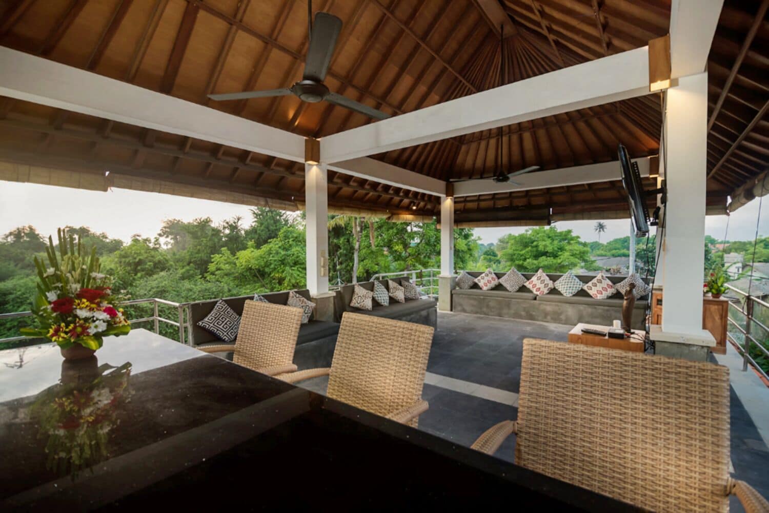 An outdoor covered seating area with wicker furniture, a table, and a ceiling fan.