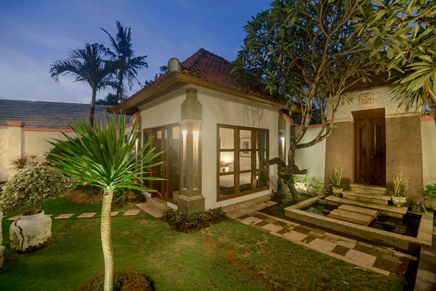 A house with a covered porch, a small garden with a palm tree, and a water feature.