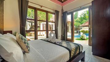 A hotel room with a bed, curtains, and a view of a swimming pool and greenery.