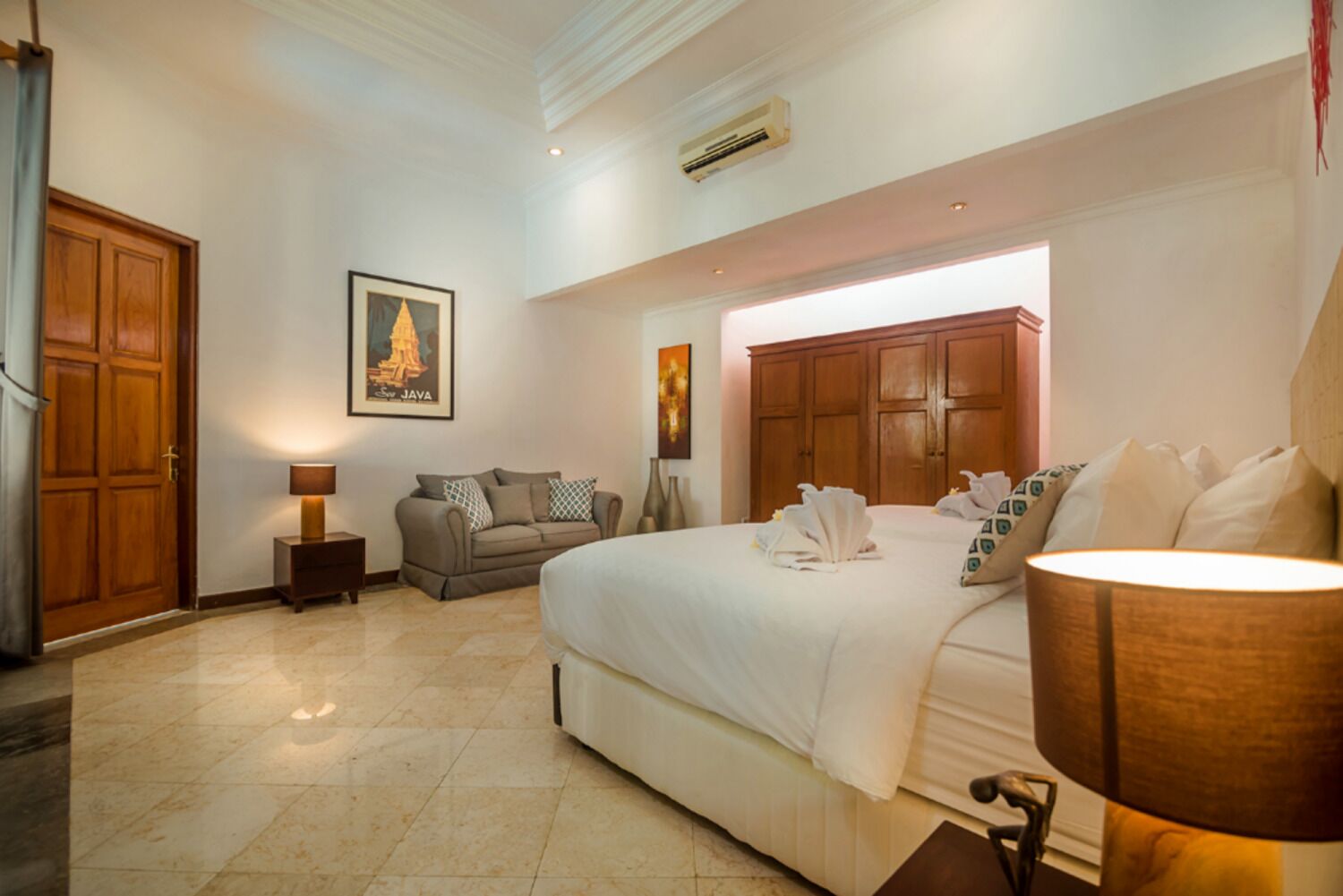 A hotel room with a large bed, a sofa, a nightstand, a lamp, and a painting on the wall.