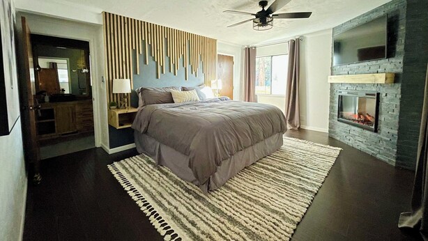 Ein modernes Schlafzimmer mit einem Bett, einem Deckenventilator, einem Kamin und einem großen Fenster.