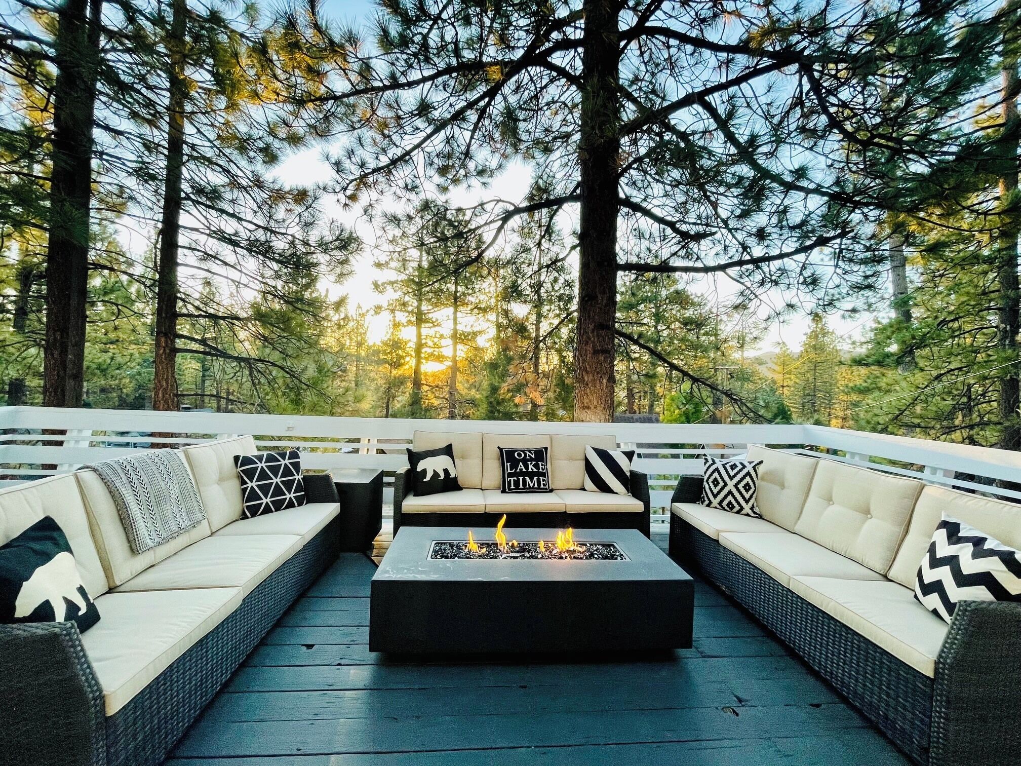 An outdoor seating area with a fire feature, surrounded by tall trees.