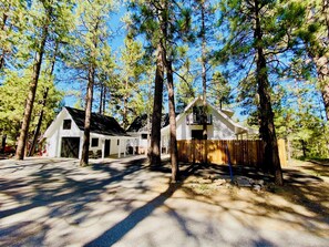 A two-story house with a covered porch and a fenced yard, surrounded by tall pine trees. - Fantastic 3-bedroom house in delightful Big Bear Lake getaway (Big Bear Lake)