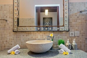 Et badeværelse med en stor stenskumvask, et spejl med dekorativ belysning og toiletartikler på bordet.