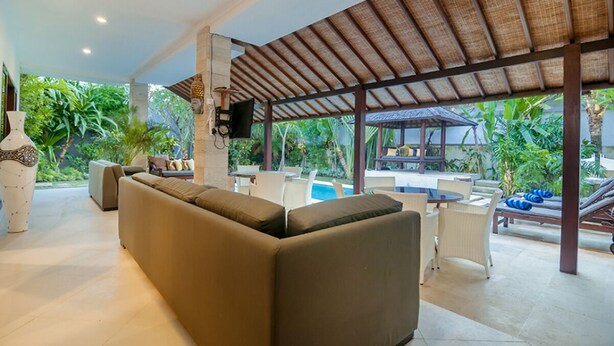 Un espacio de estar techado al aire libre con un sofá, sillas y una piscina.