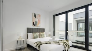 Une chambre à coucher moderne avec un grand lit, une table de chevet, une lampe et une vue sur l’extérieur.